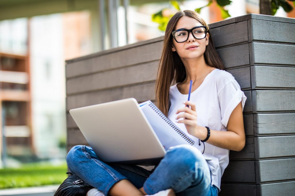 Happy young woman in casual outfit and glasses using modern laptop.